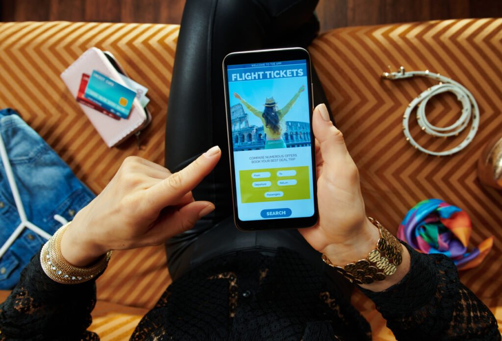 person sitting on sofa in modern living room booking airplane tickets online on a smartphone using airline rewards credit cards