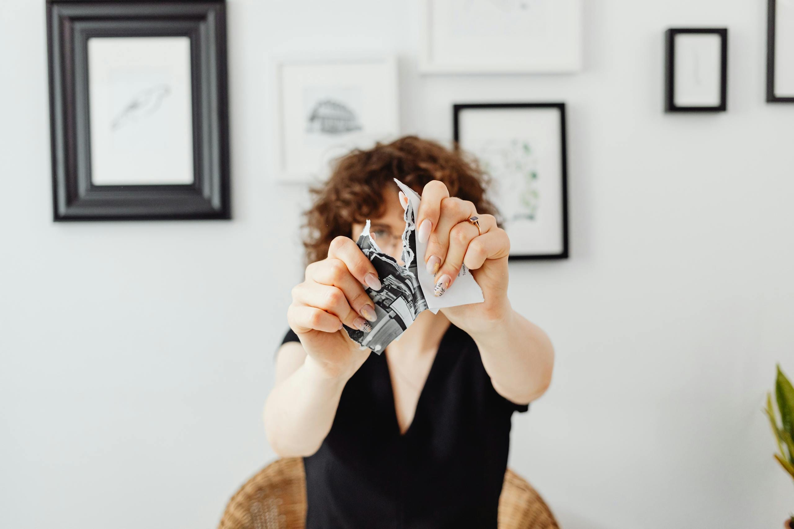 A woman tearing a paper in front of several framed art pieces, creating a dramatic and symbolic moment.